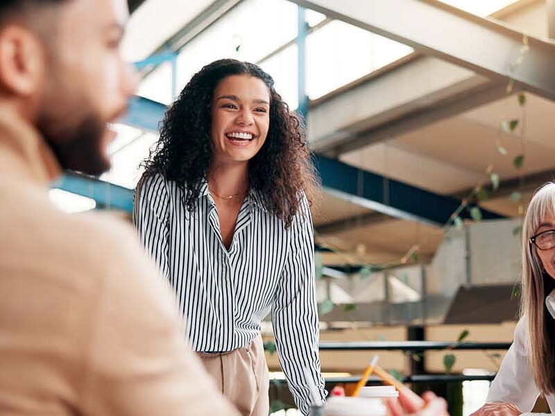 A diverse group of people smiling and collaborating during a meeting in a bright, modern office space.