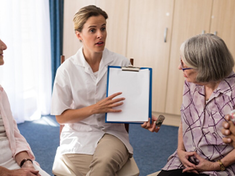 medical professional with clipboard in hand speaking to a group of elderly people